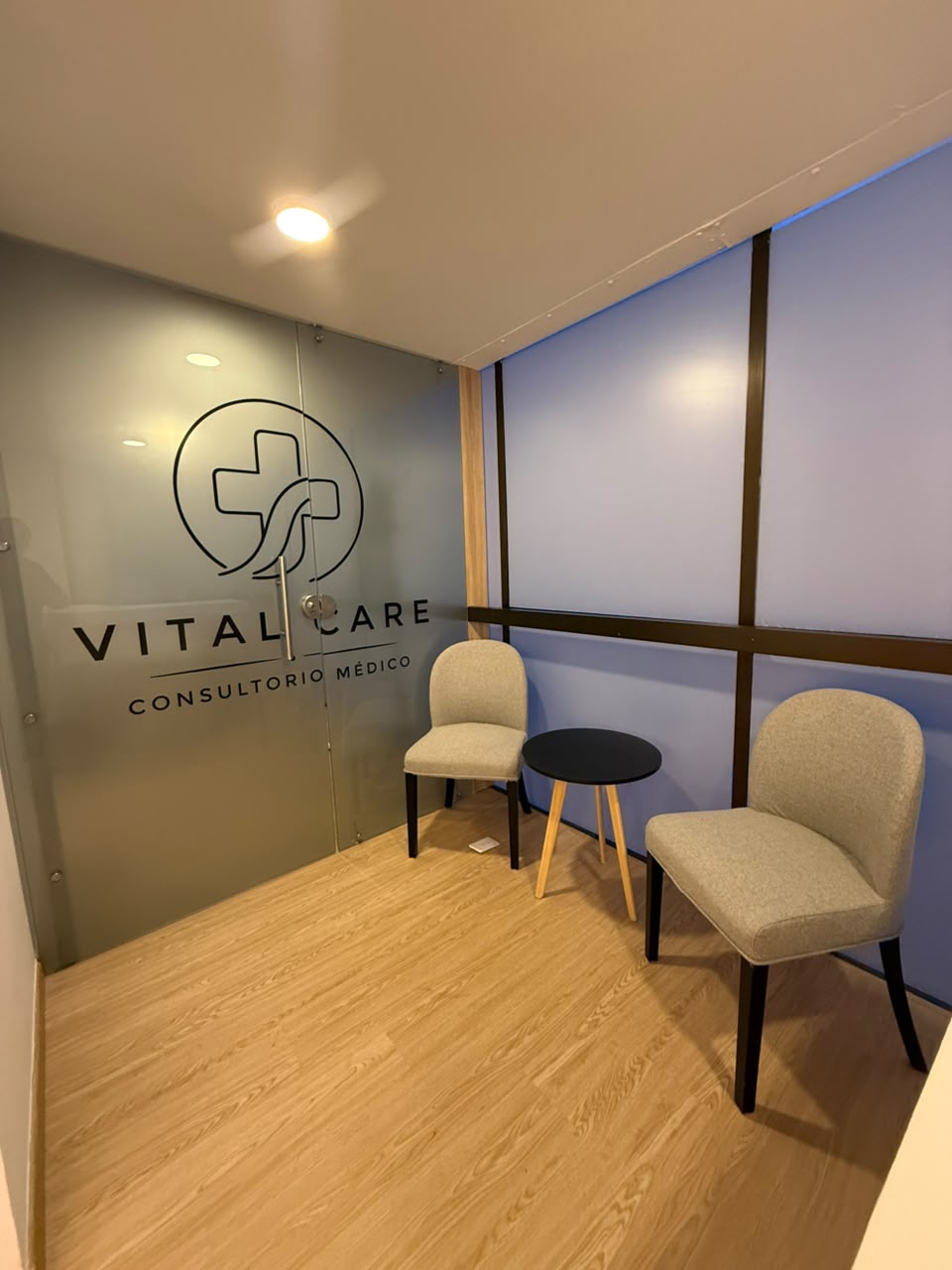 Zona de espera con butacas y puerta de vidrio con el logo de Vital Care