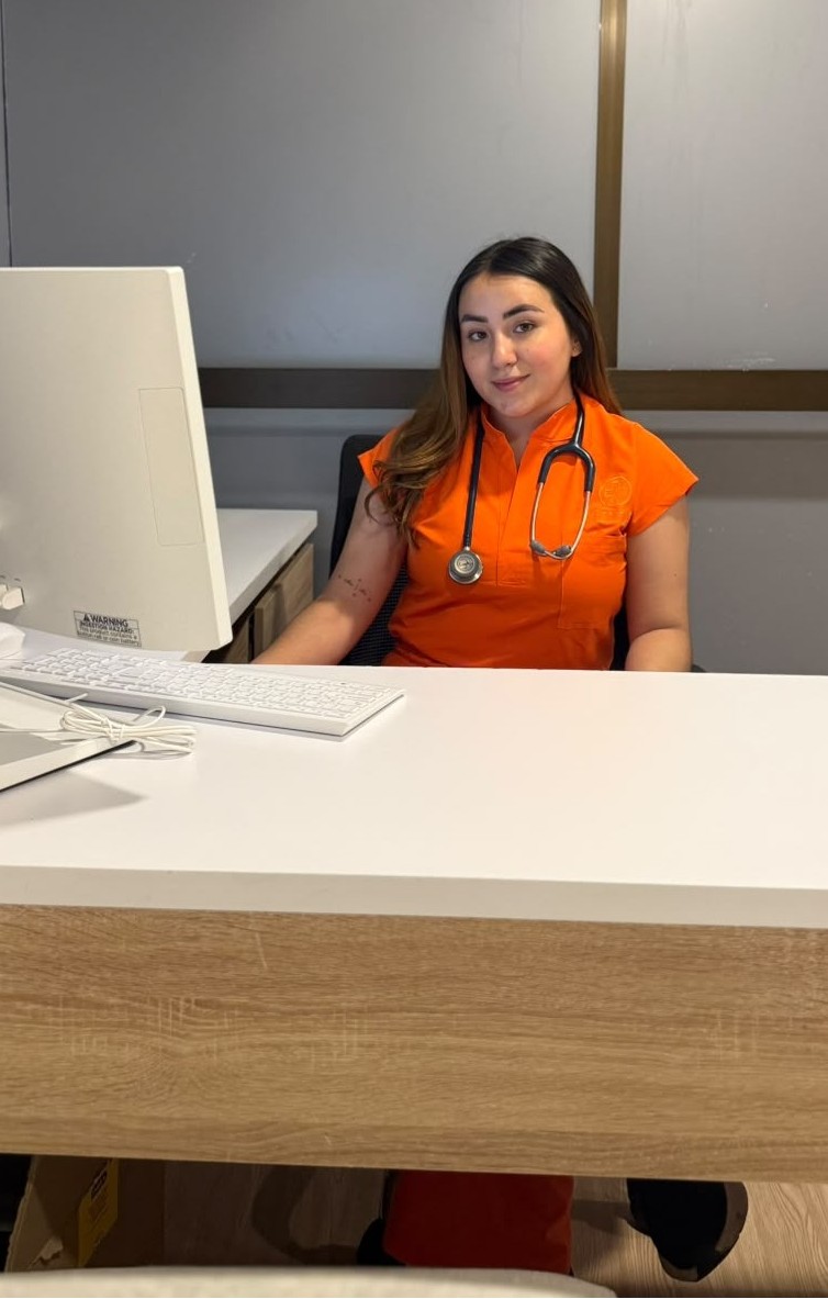 Profesional de la salud de Vital Care con uniforme médico naranja y estetoscopio, sentada tras su escritorio en el consultorio